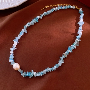 Detail of aquamarine chips necklace with baroque pearl on brown satin background
