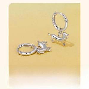 Detailed view of S925 sterling silver dachshund puppy earrings on a soft yellow background