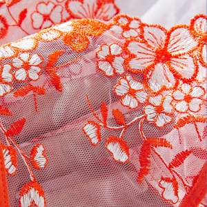 Macro shot of delicate orange and white floral embroidery on semi-transparent mesh lace