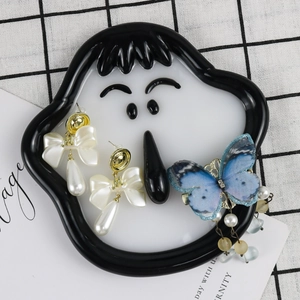 Flat lay of resin bow pearl earrings and blue fabric butterfly hairclip in cartoon tray