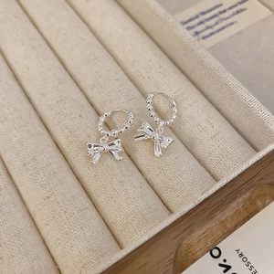 Macro shot of silver bow pendant earrings with beaded hoop detail on beige jewelry box