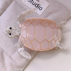 Detail of a pink sea turtle hair claw clip with golden veins and white textured limbs