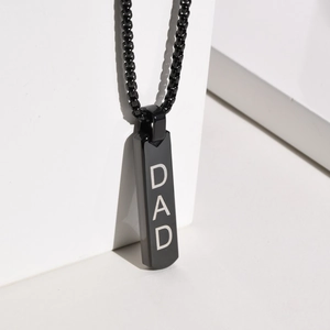 Close-up of black rectangular bar necklace with DAD engraving on white geometry base