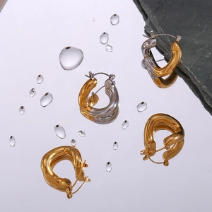Detailed macro view of polished twisted metal earrings on a mirror base with water droplets
