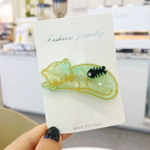 Cute green cat-shaped hair clip with gold edges and pearl accents on a display card