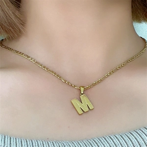 Dettaglio di una collana con ciondolo a lettera M dorata testurizzata sul collo