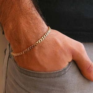 Close-up of a gold-plated Cuban link chain bracelet worn on a male wrist over grey denim