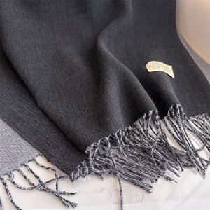 Close-up of dual-color cashmere-style scarf with fringe detail and woven brand label