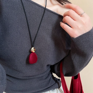 Detail of red velvet teardrop pendant and golden metal buckle on long sweater chain