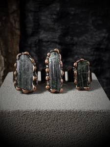 Detailed close-up of three vintage irregular raw green tourmaline rings on copper bands