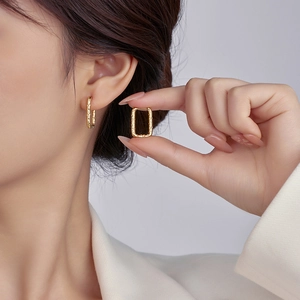 Close-up of golden rectangular textured earrings worn by a model with a clean backdrop