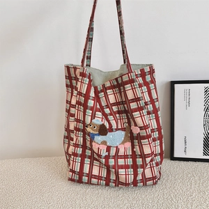Detail of red and green plaid tote bag featuring embroidered cartoon puppy on soft rug