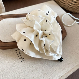Détail d'une pince à cheveux fleurie beige à pois en satin sur un plateau en bois