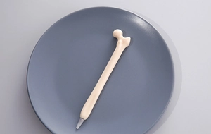 Close-up of a creative bone-shaped ballpoint pen on a dark gray circular tray