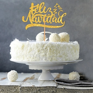 Close-up of golden glitter Feliz Navidad cake topper with tree on white coconut cake