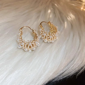 Detail of gold-plated hoop earrings with white pearls on a soft white plush background
