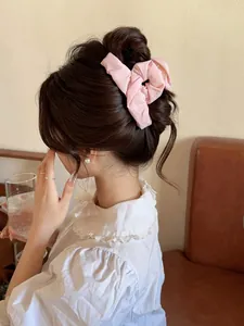 Detail of pink pleated fabric bow clip worn on a bun hairstyle in a cozy indoor setting