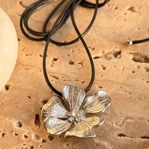Macro detail of 18k gold flower pendant with zircons on textured stone background