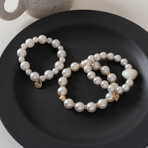 Detail of vintage elastic pearl bracelets with heart and circular charms in a black tray