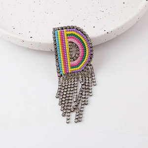 Detail of colorful embroidered letter D brooch with sparkling rhinestone fringe tassels