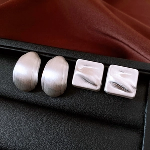 Détail macro de boucles d'oreilles argentées géométriques sur présentoir en cuir noir