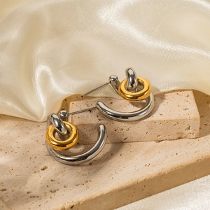 Close-up of two-tone gold and silver C-shaped earrings on beige stone and champagne silk