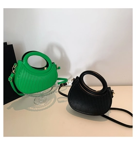 Close-up of pleated saddle bags in green and black with round handles on glass display