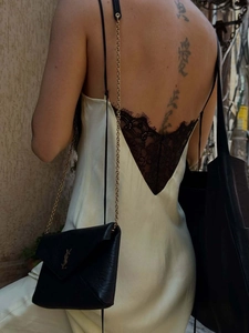 Detail of elegant backless cream satin dress with intricate black lace trim and chain bag
