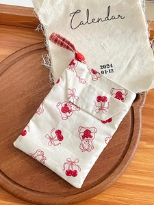 Detail of cute white fabric pouch with red bear and cherry patterns on wood tray