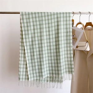 Detail of green and white plaid scarf with fringe tassels on a minimalist hanger