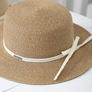 Detail of high-quality raffia straw weave with ivory ribbon bow and metal brand logo