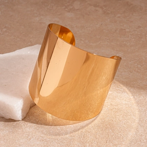 Gros plan d'un large bracelet doré ouvert avec finition miroir sur une pierre blanche