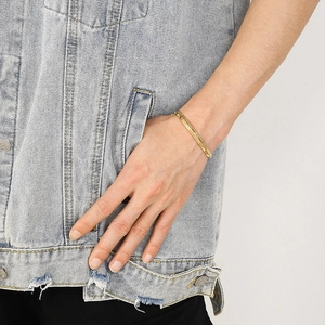 Detail of a gold geometric C-shaped bangle on a wrist with a casual denim outfit