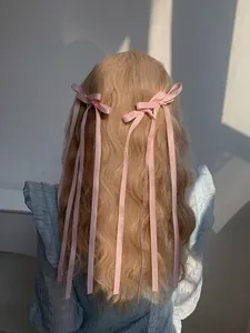 Detailed back view of pink satin bow hair clips with long tassels on wavy blonde hair