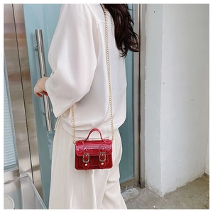 Glossy red mini jelly bag with gold chain strap shown on model in outdoor setting