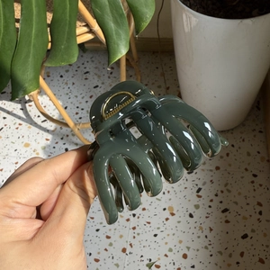 Detail of a large dark green glossy resin hair claw clip held in hand with natural light