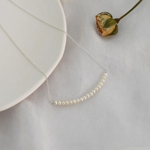 Elegant freshwater pearl smile necklace in silver, minimalist style on white ceramic plate