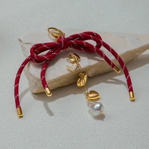 Detail of red bow keychain with golden heart charms and a large baroque pearl on a stone