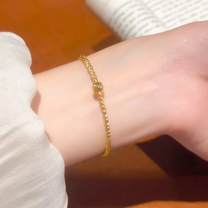 Detailed view of 24K gold plated beaded bracelet on model's wrist in warm lighting