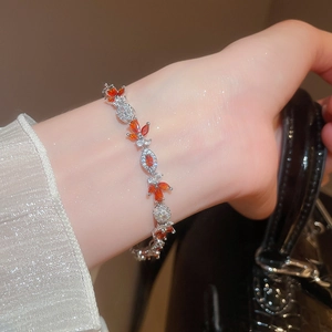 Elegant leaf bracelet with orange and white zircon stones worn on wrist with black bag