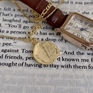 Golden irregular wavy pendant necklace and vintage square watch set on book pages