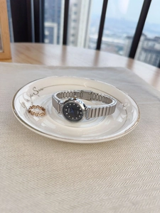 Close-up of women's silver mesh watch with black rhinestone dial and gold wave ring