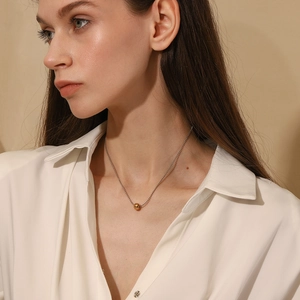 Elegant gold bead pendant on a silver chain necklace worn by a model in a white shirt