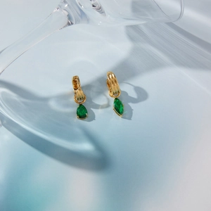 Dettaglio di orecchini a cerchio dorati con texture verticale e pendente in zircone verde