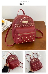 Detailed view of red mini backpack with golden rivets and rhinestone accents on wood