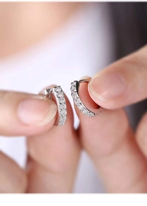 Macro detail of silver-toned huggie hoop earrings with micro-paved cubic zirconia
