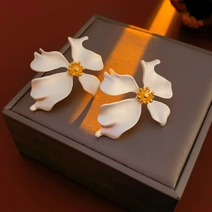 Detailed close-up of matte white flower earrings with gold centers on a jewelry box