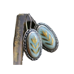 Elegant oval blue enamel drop earrings with gold floral design on a rustic wooden frame