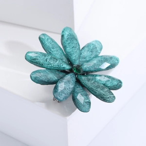 Detailed close-up of teal acrylic flower brooch with resin texture on white podium