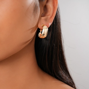Close-up of a model wearing a thick golden C-shaped hoop earring with a polished mirror finish